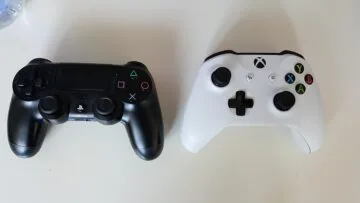 Black PlayStation 4 controller and white Xbox One controller placed side by side on a table