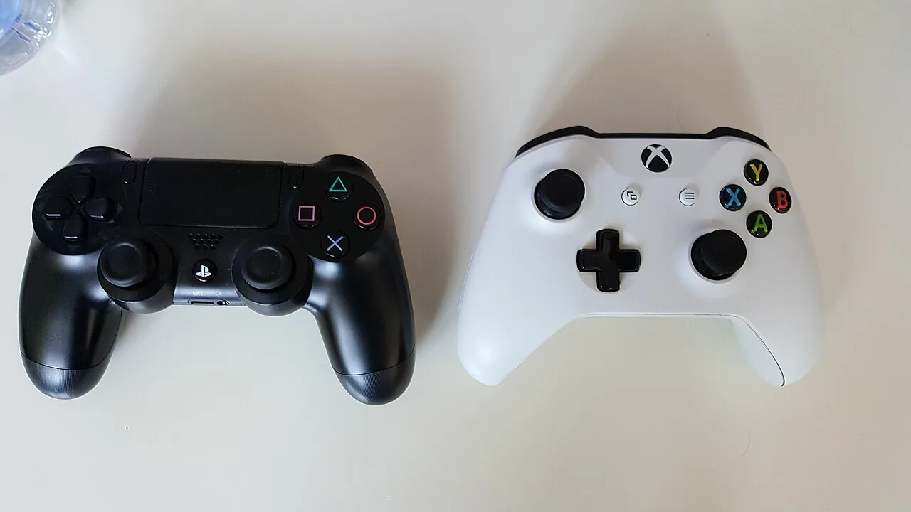 Black PlayStation 4 controller and white Xbox One controller placed side by side on a table